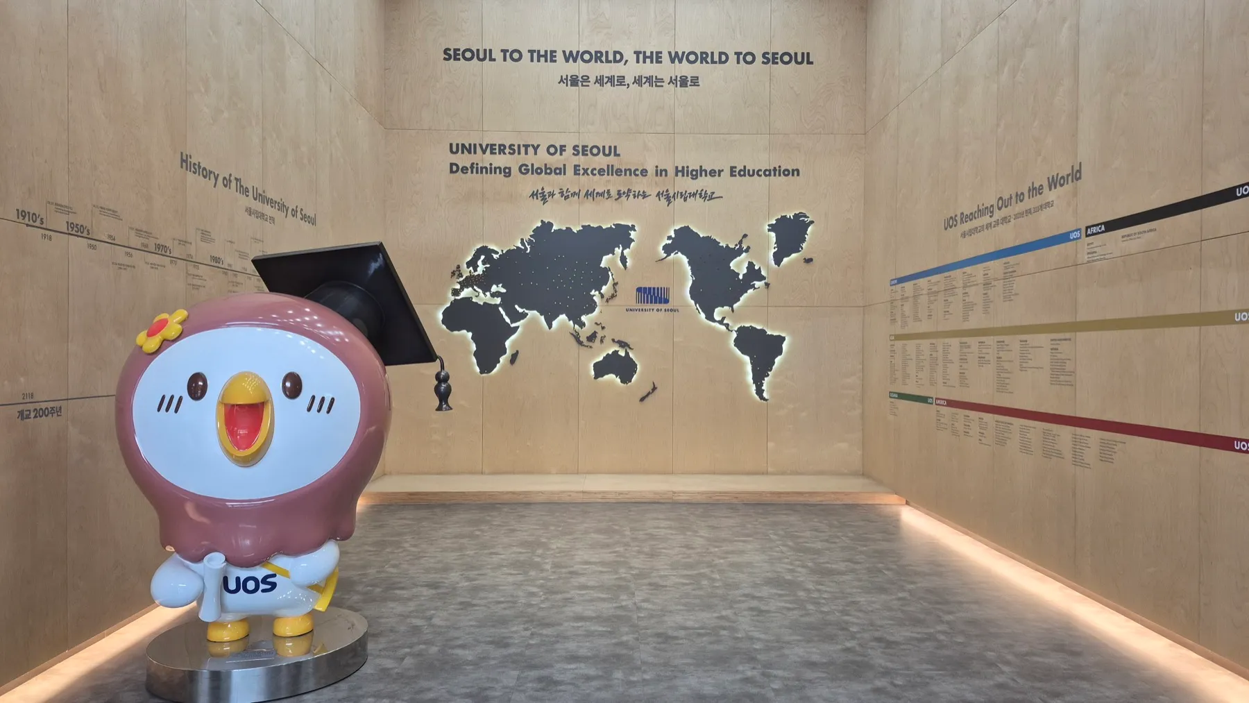 디지털배지 발급기관 서울시립대학교(University of Seoul)의 브랜드월. UOS 마스코트 조형물과 '서울은 세계로, 세계는 서울로' 세계지도가 보인다