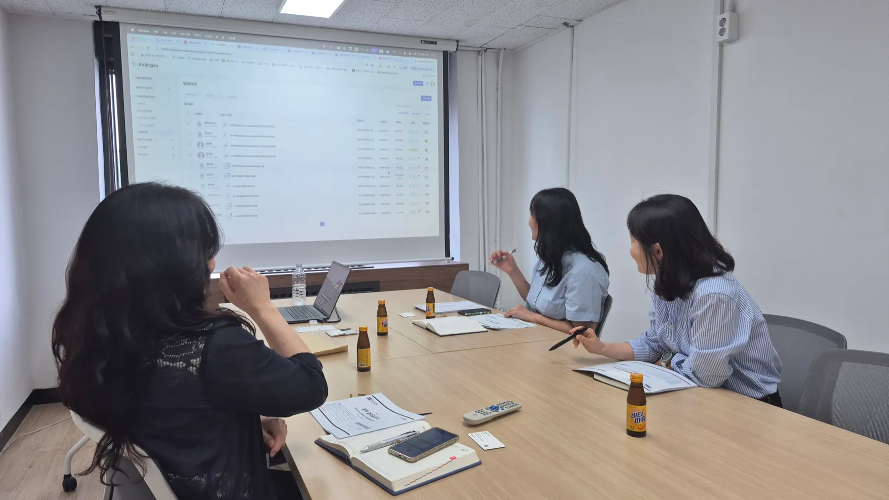 서울시립대학교 산학협력단 담당자들이 회의실 화면의 칼리지스 관리자 포털 디지털배지 발급 내역(수령자·인증서·발급일·상태)을 함께 검토한다